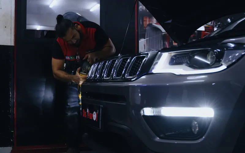 Técnico da Dr. Farol trabalhando na frente de um Jeep com os faróis acesos